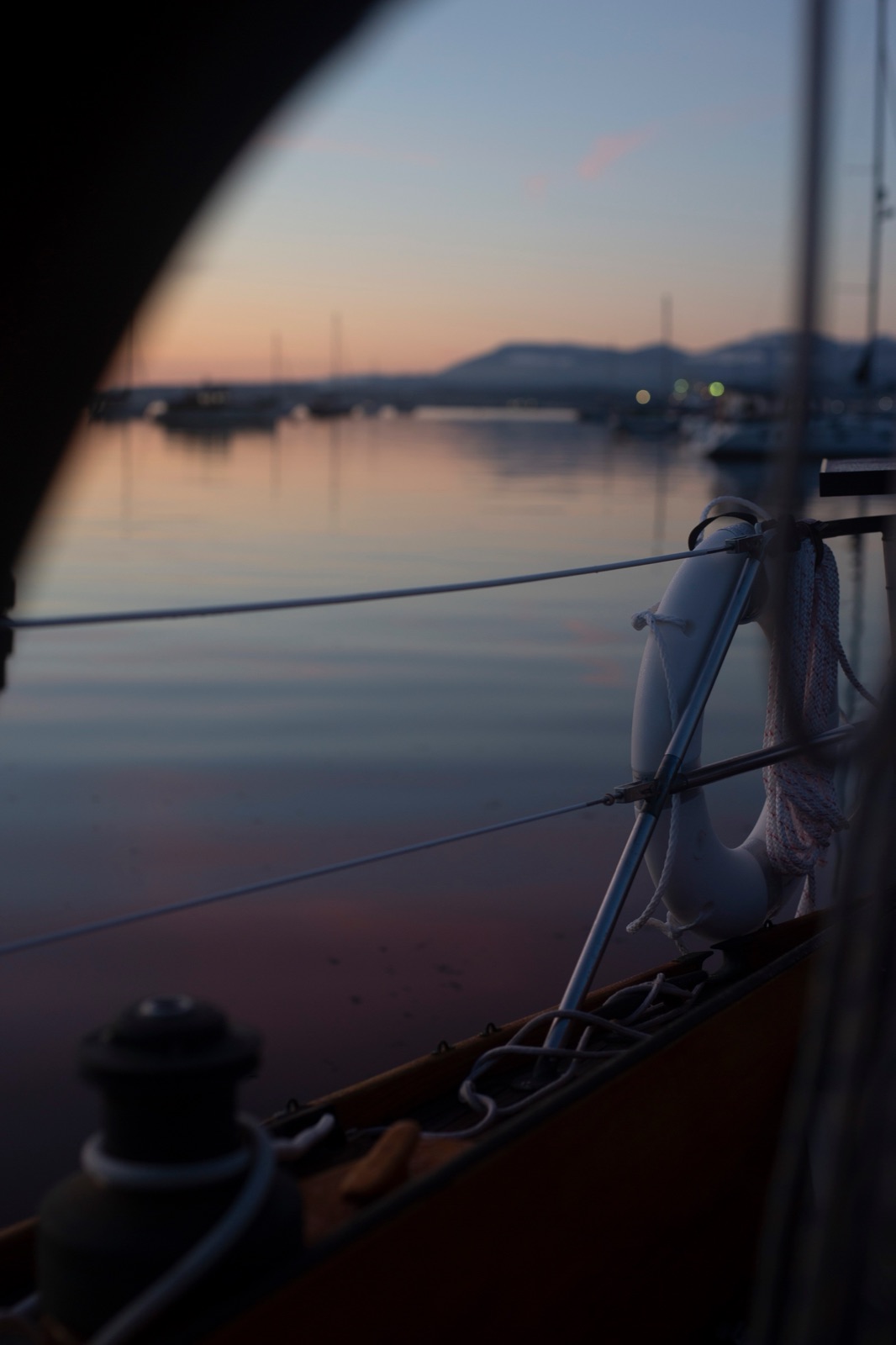 Dusk through the shrouds at anchor, harbour lights along the shore